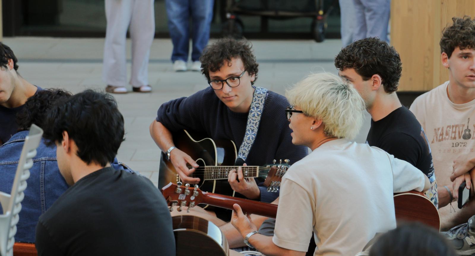 A group of students sitting in the center of the Contemplative Commons Gingko Garden Courtyard while playing guitars. 