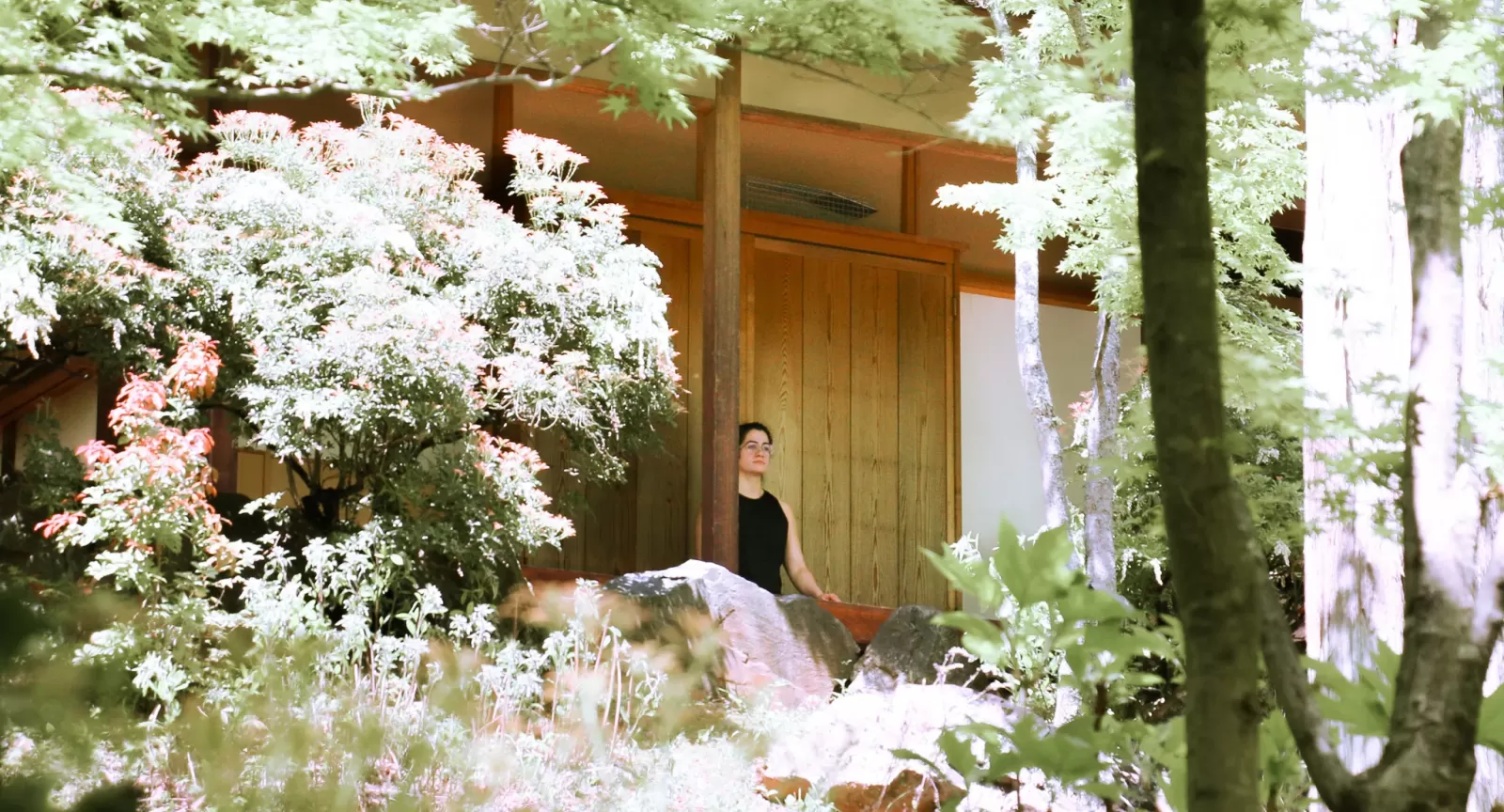 Person meditating on covered deck of a cabin surrounded by blooming trees