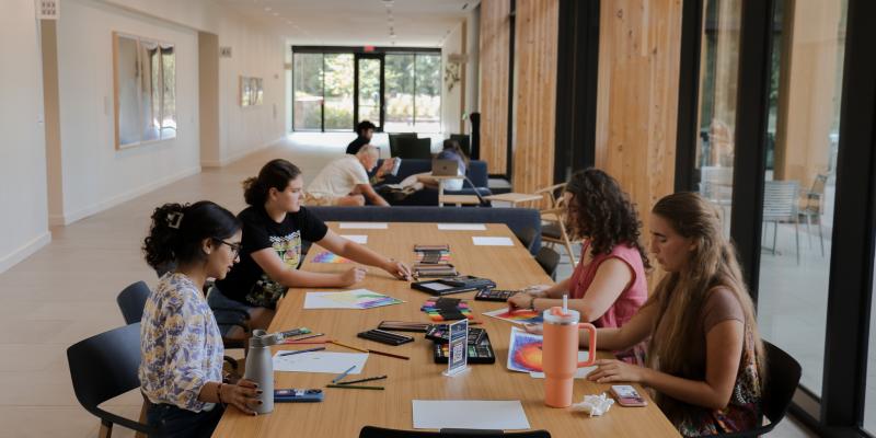 Four students painting in the Contemplative Commons first floor gallery. More students are further back in the hallway. 