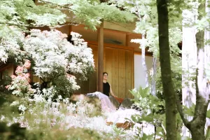 Person meditating on covered deck of a cabin surrounded by blooming trees