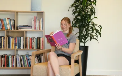 Student reading in the Contemplative Commons with a bookshelf and plant in the background