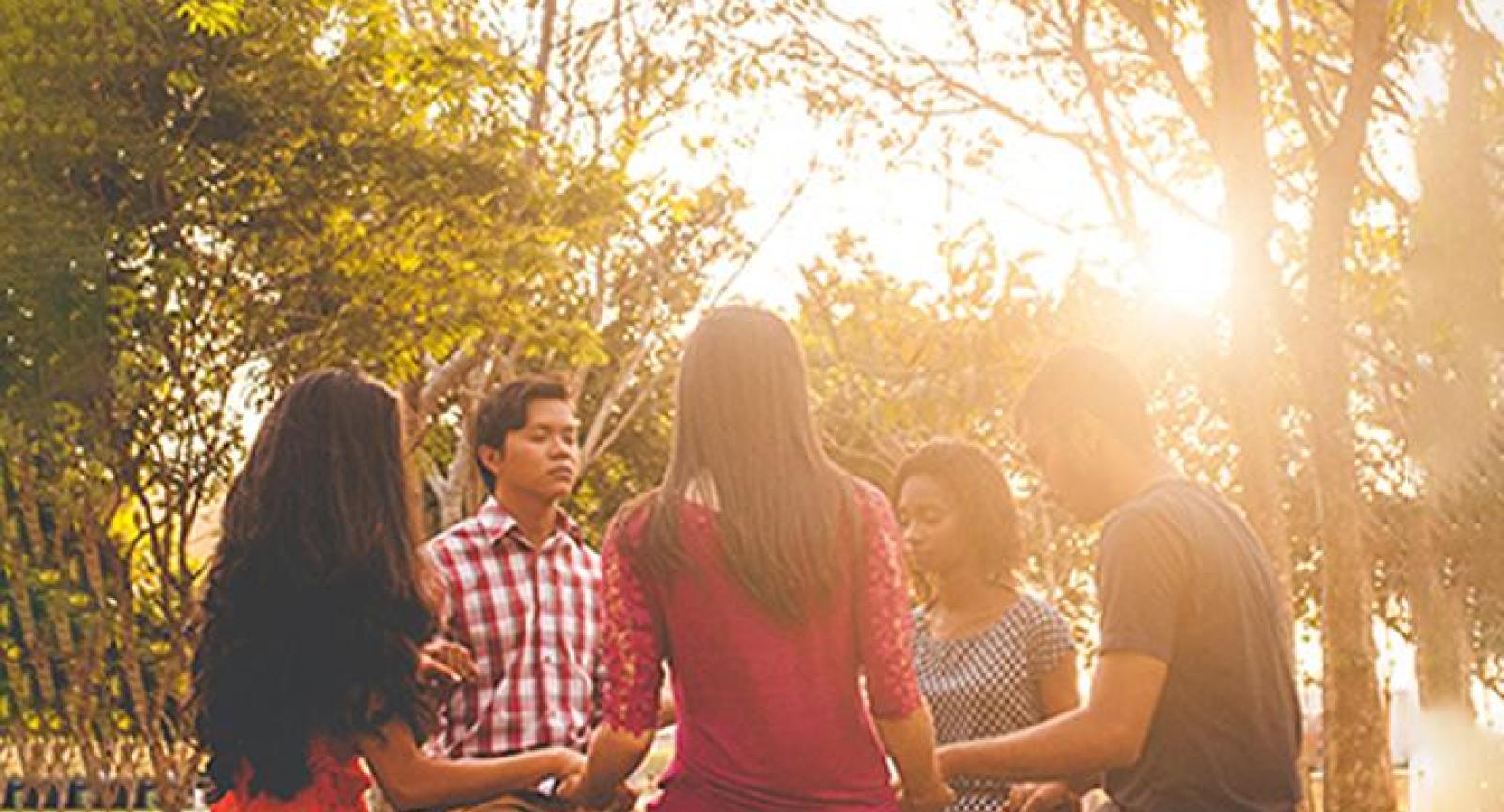 A group of student standing in a circle holding hands with eyes closed