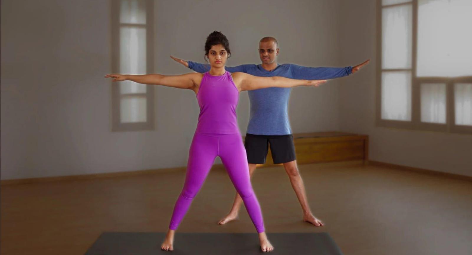 A woman in pink and a man in blue doing yoga in a studio