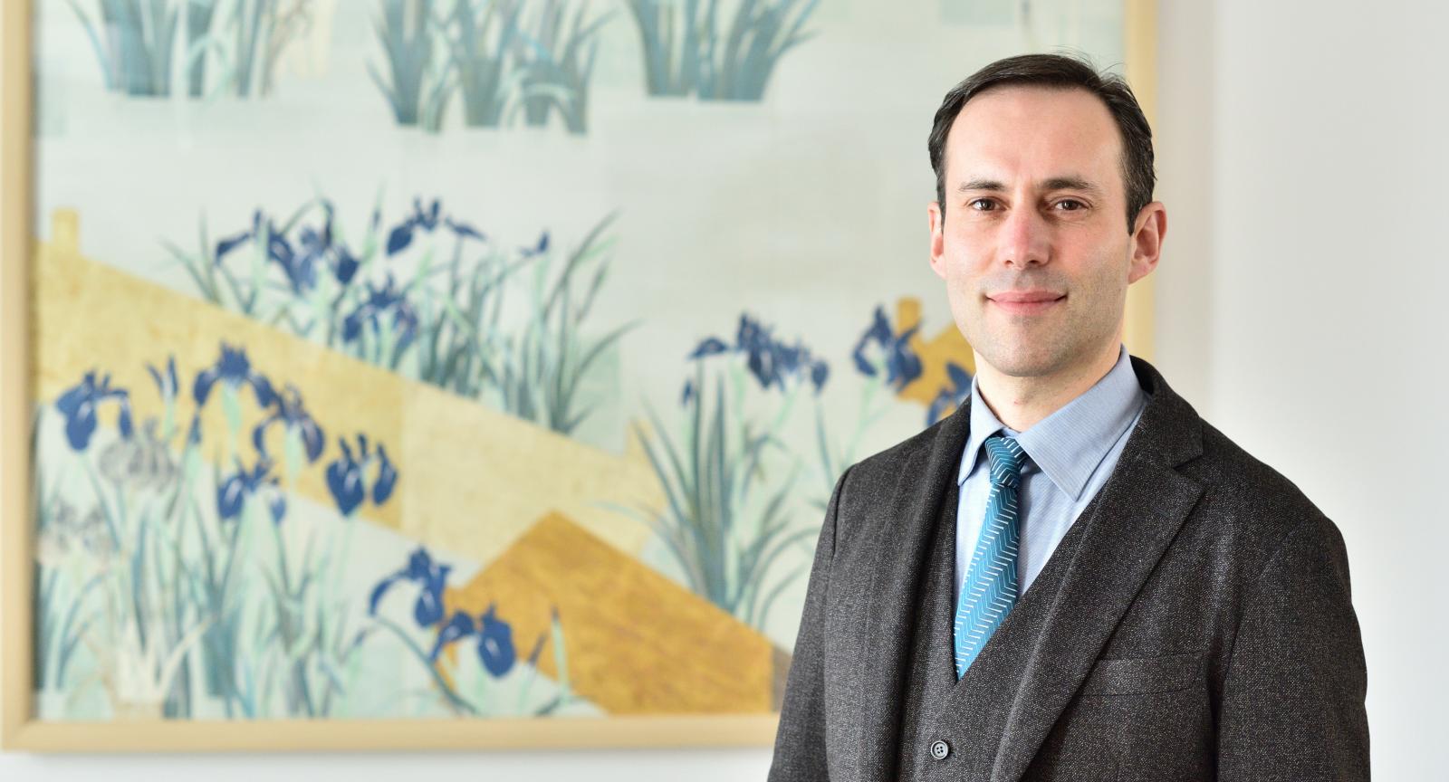 Marc-Henri Deroche stand in front of a painting wearing a suit