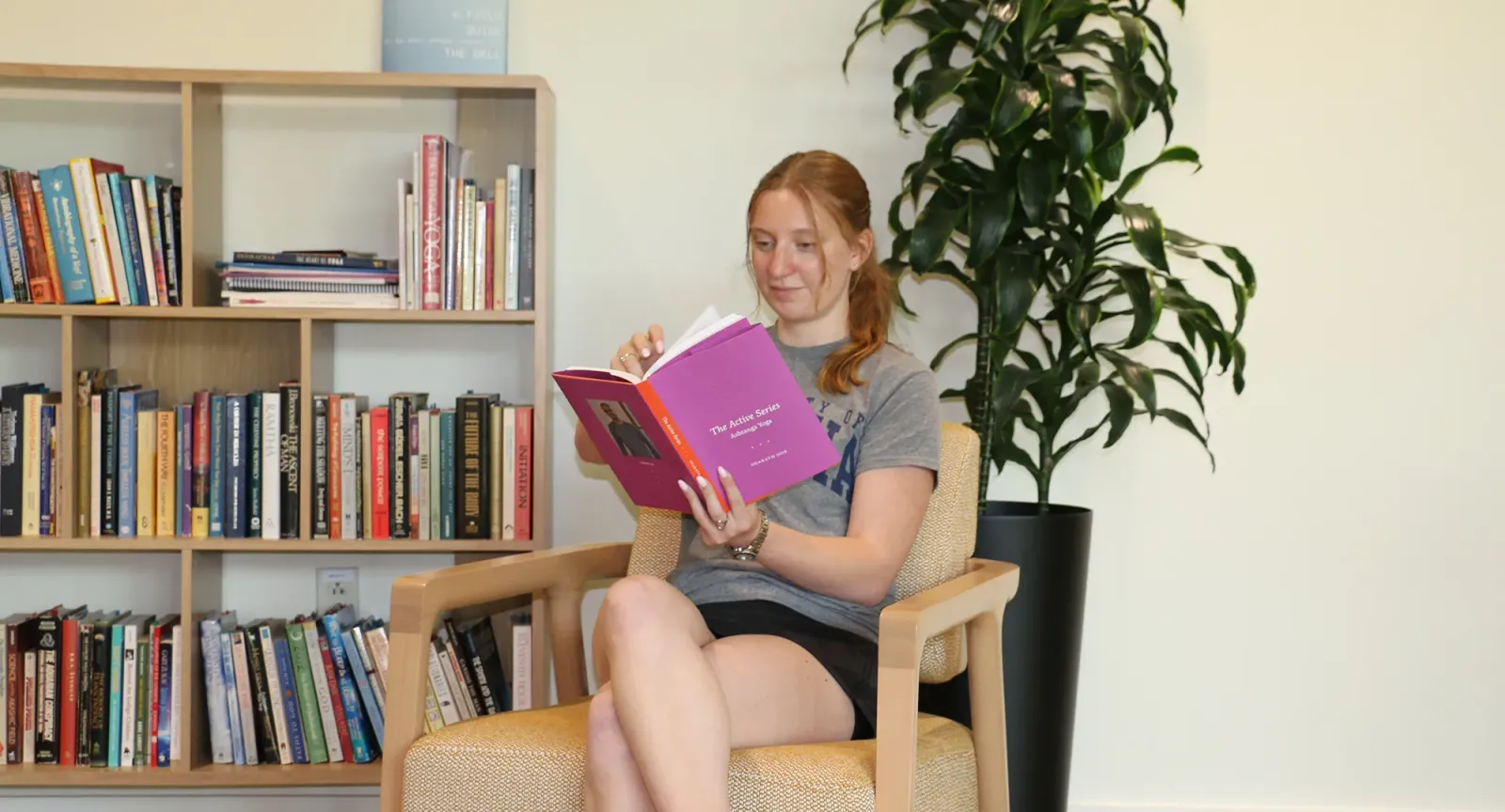 Student reading in the Contemplative Commons with a bookshelf and plant in the background