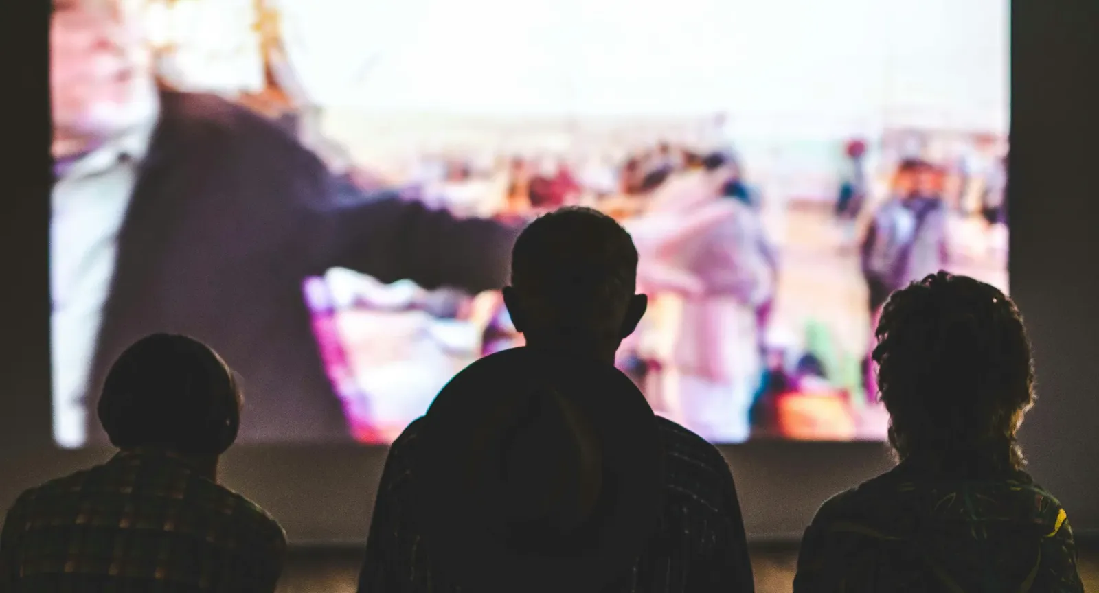 Three silhouettes of people watching a movie