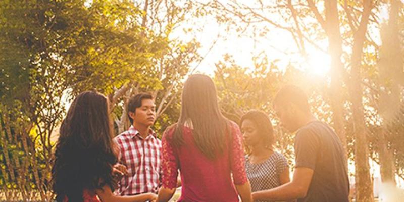 A group of student standing in a circle holding hands with eyes closed