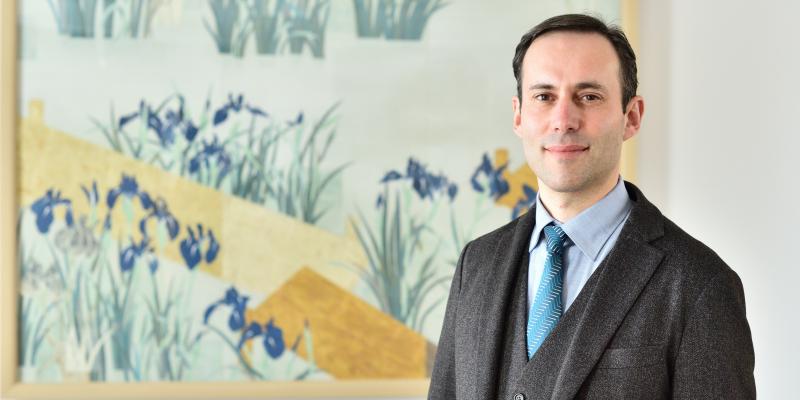 Marc-Henri Deroche stand in front of a painting wearing a suit