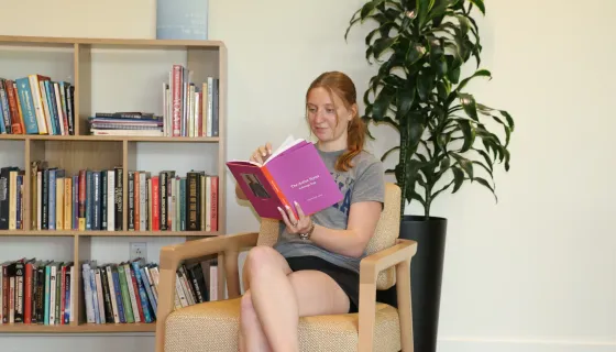 Student reading in the Contemplative Commons with a bookshelf and plant in the background