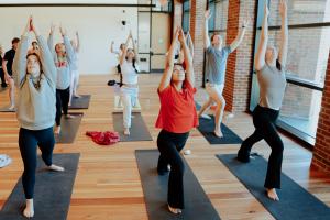 Students practice Ashtanga Yoga, reaching their arms up towards the ceiling in a room with wooden floors