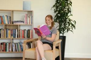 Student reading in the Contemplative Commons with a bookshelf and plant in the background