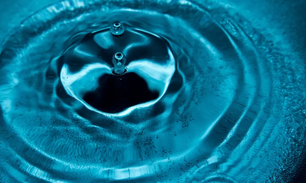 drops splashing in florescent blue water creating a ring of ripples