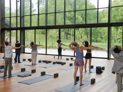 People stretching in front of yoga mats in the Contemplative Commons looking out at summer greenery