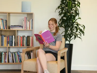 Student reading in the Contemplative Commons with a bookshelf and plant in the background